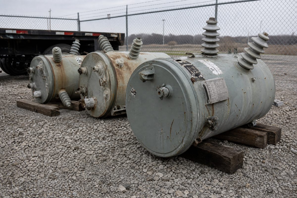 Used pole-mount transformers stacked in a utility surplus yard