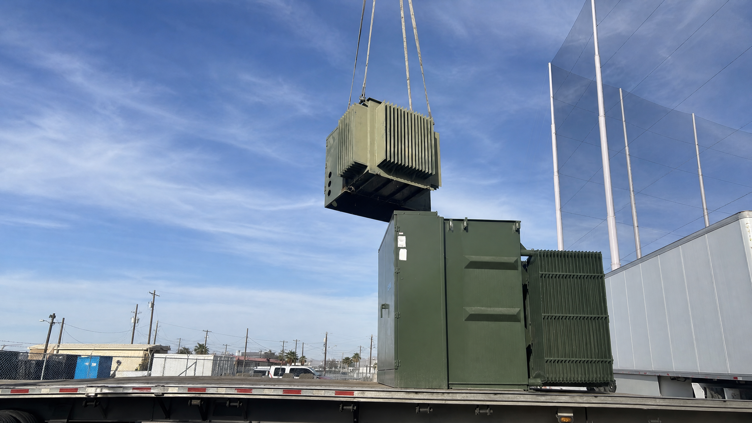 Green padmount transformer being lifted by a crane over a flatbed truck