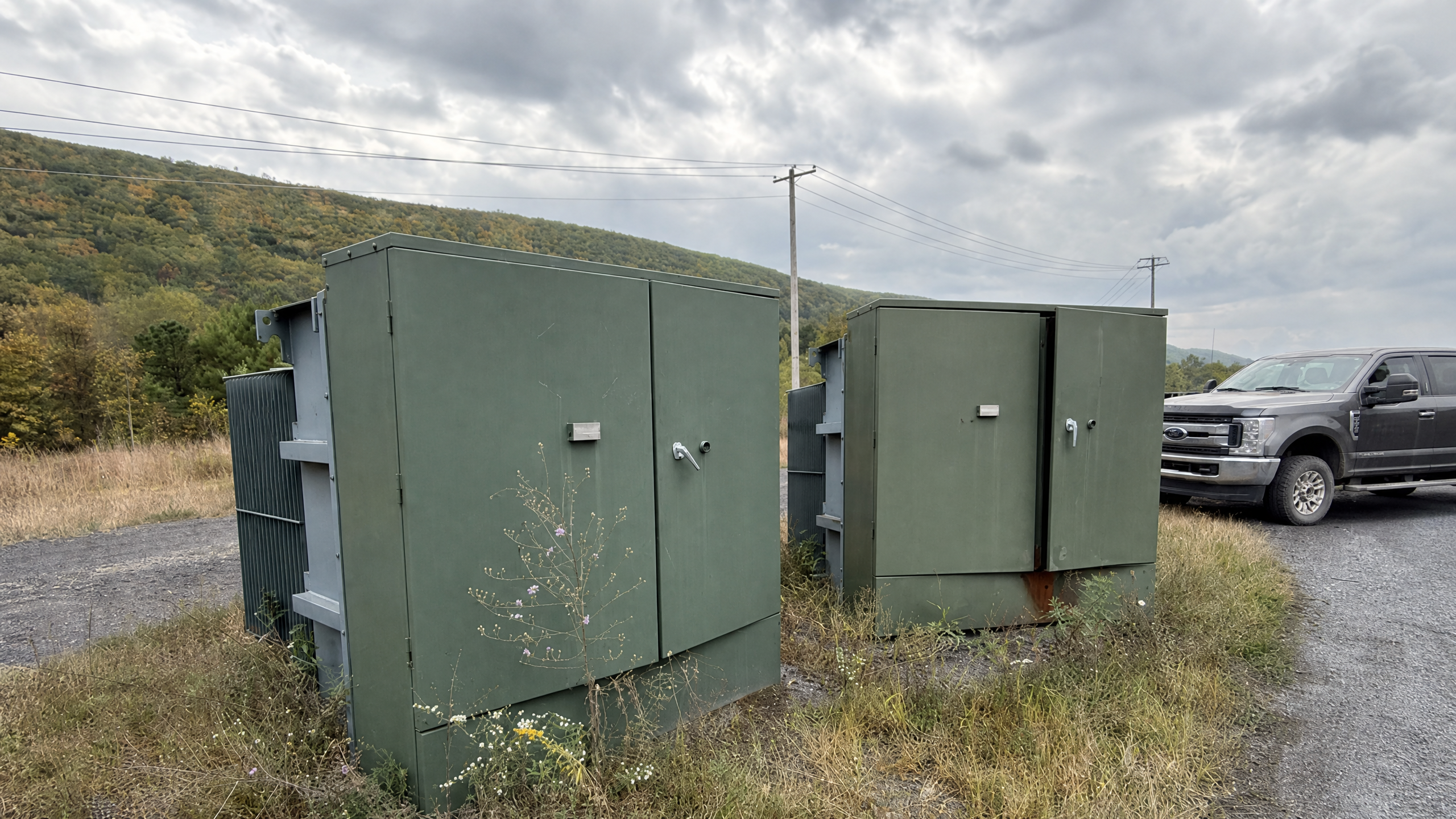Two green padmount transformers installed beside a gravel access road