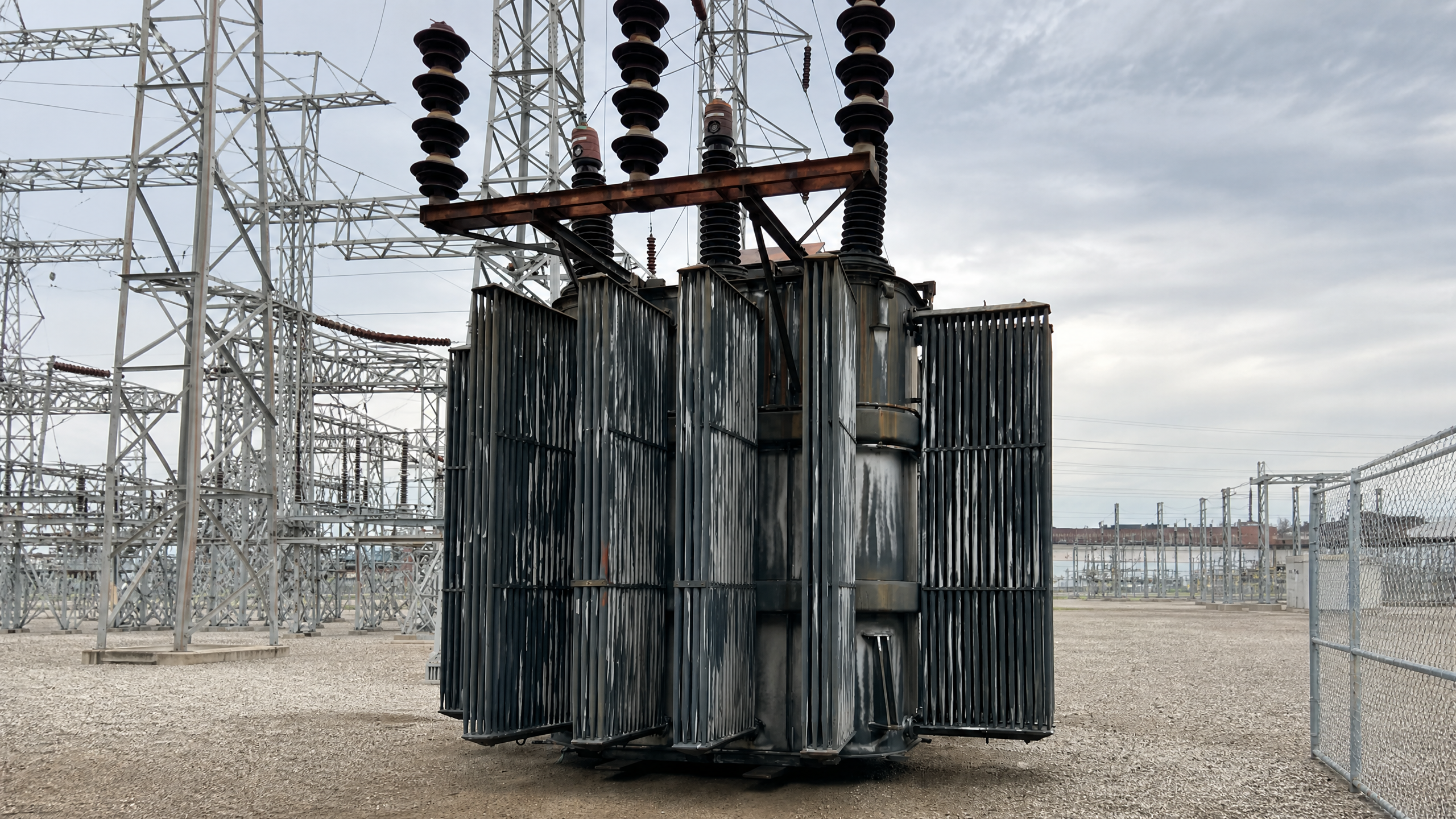 Large weathered electrical transformer with cooling fins in a substation yard